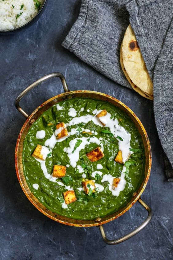 Palak paneer (spinach and cheese) in a copper pan, garnished with cream, alongside rice and naan.
