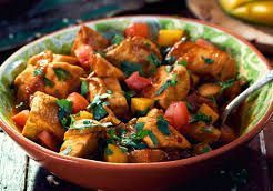 Chicken curry in a decorative bowl with tomatoes, mango, and cilantro; close-up.