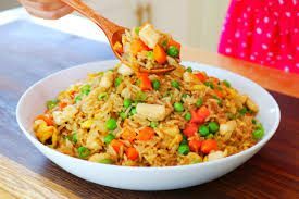 Bowl of colorful fried rice with carrots, peas, and chicken being scooped by a wooden spoon.