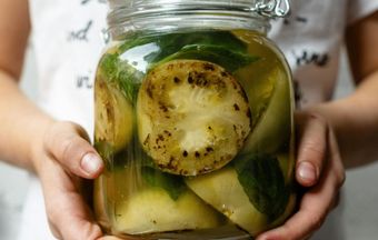 Hands holding a jar of pickled green tomatoes and herbs in brine.