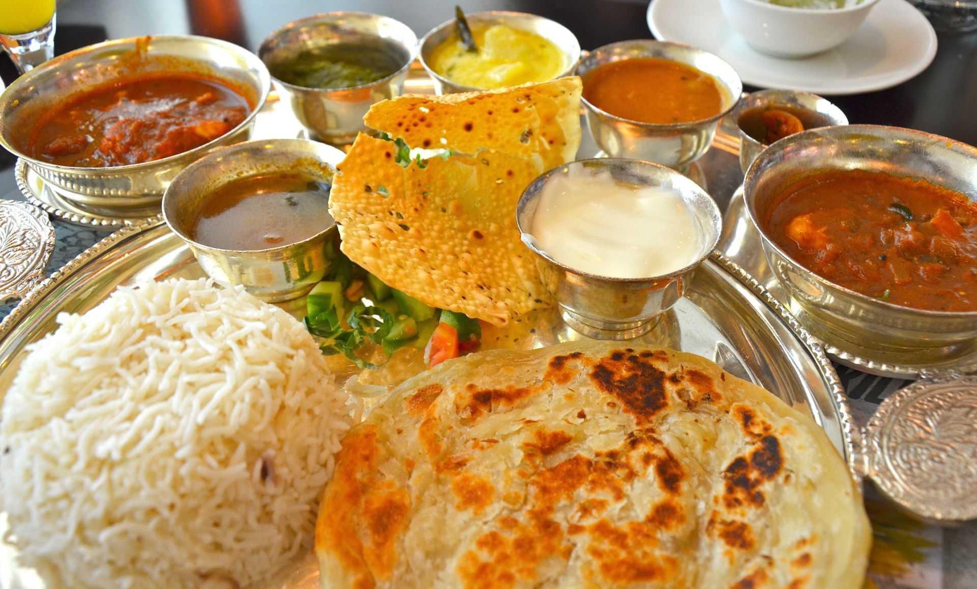 Indian thali: Assorted curries, rice, bread, and dosa arranged on a silver platter.
