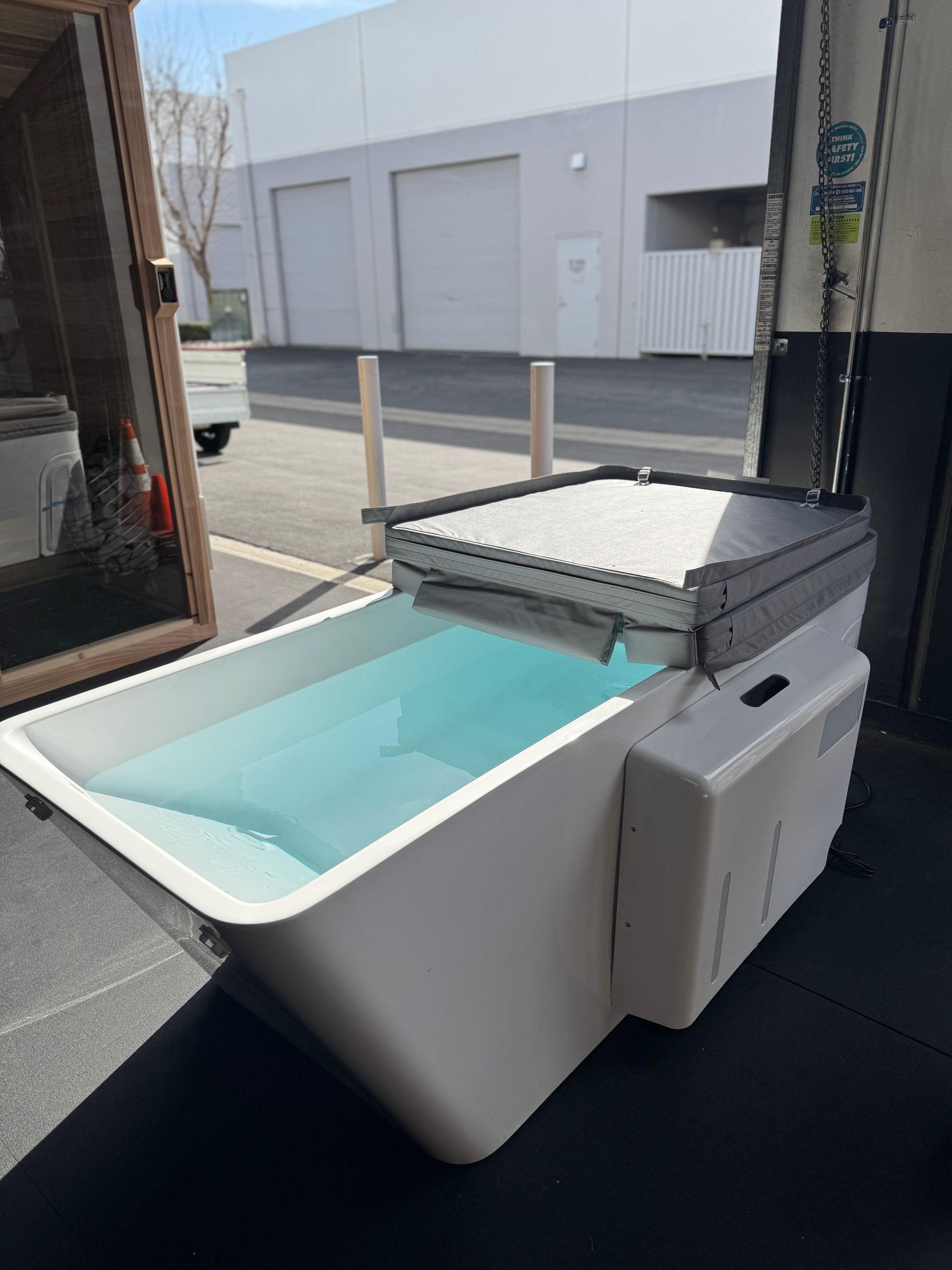 A white tub filled with blue water is sitting on the ground in front of a building.