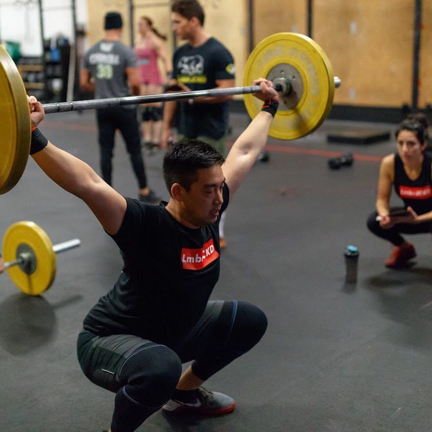 A man squats down while lifting a barbell in a gym