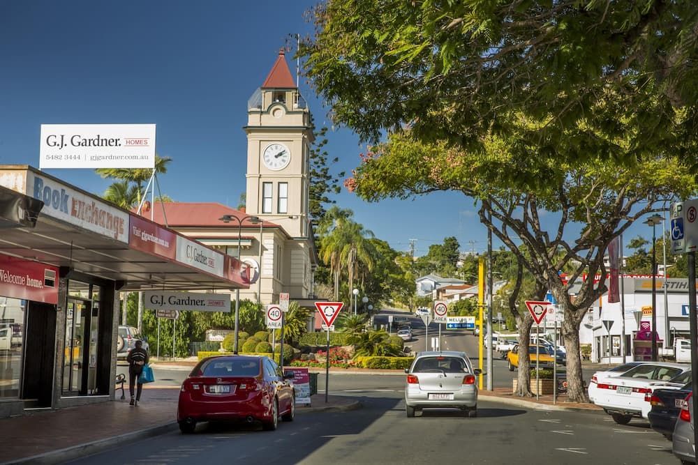 A City Street With Cars Driving Down It and a Clock Tower in the Background — Alert Smoke Alarm Compliance in Gympie, QLD