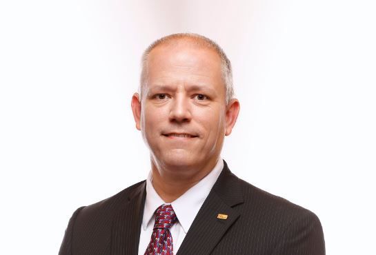 A man in a suit and tie is standing in front of a white background.