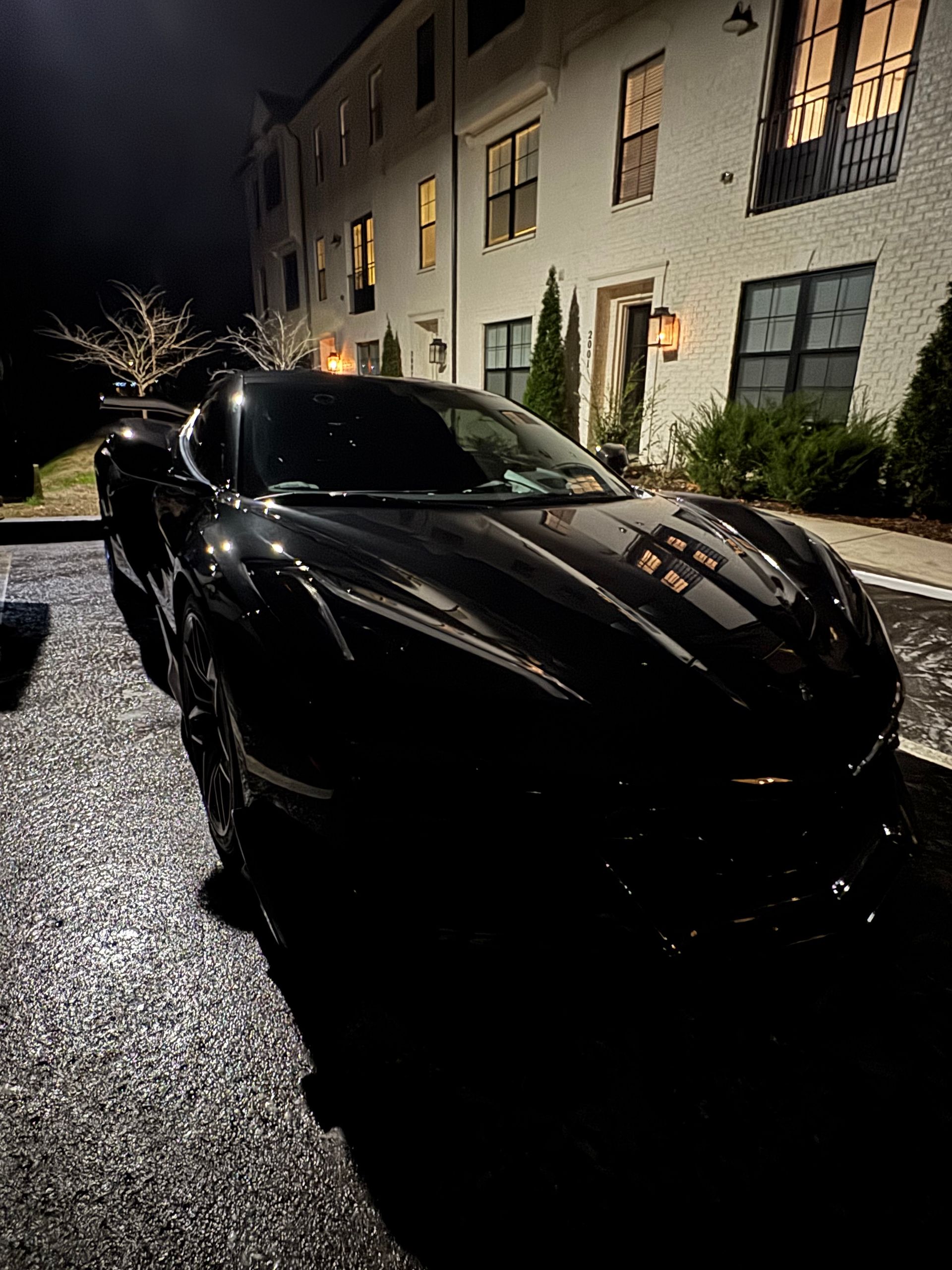 Black sports car parked at night in front of a brick building with lit windows.