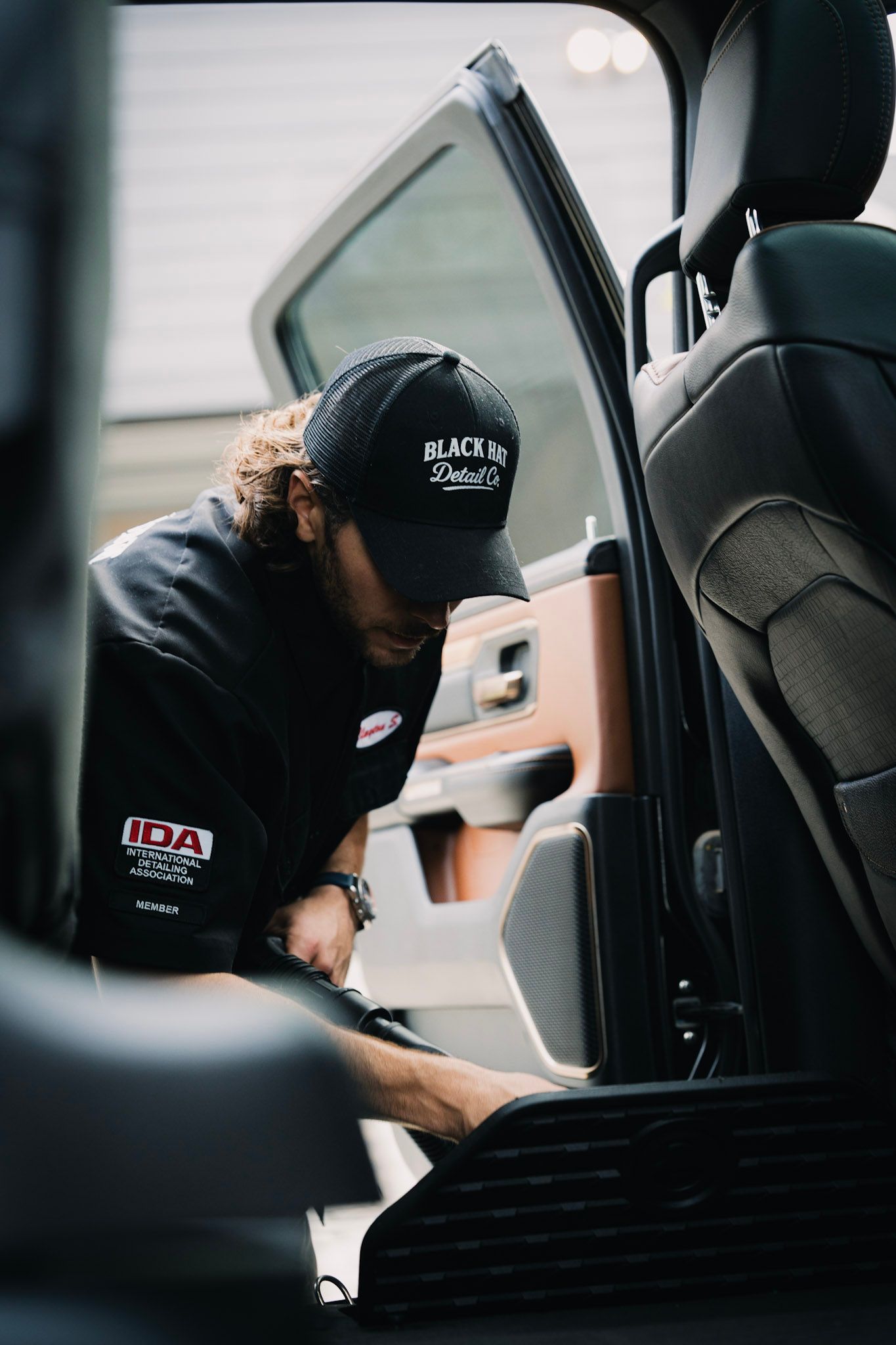 Person wearing a cap and black shirt cleaning a car's interior.