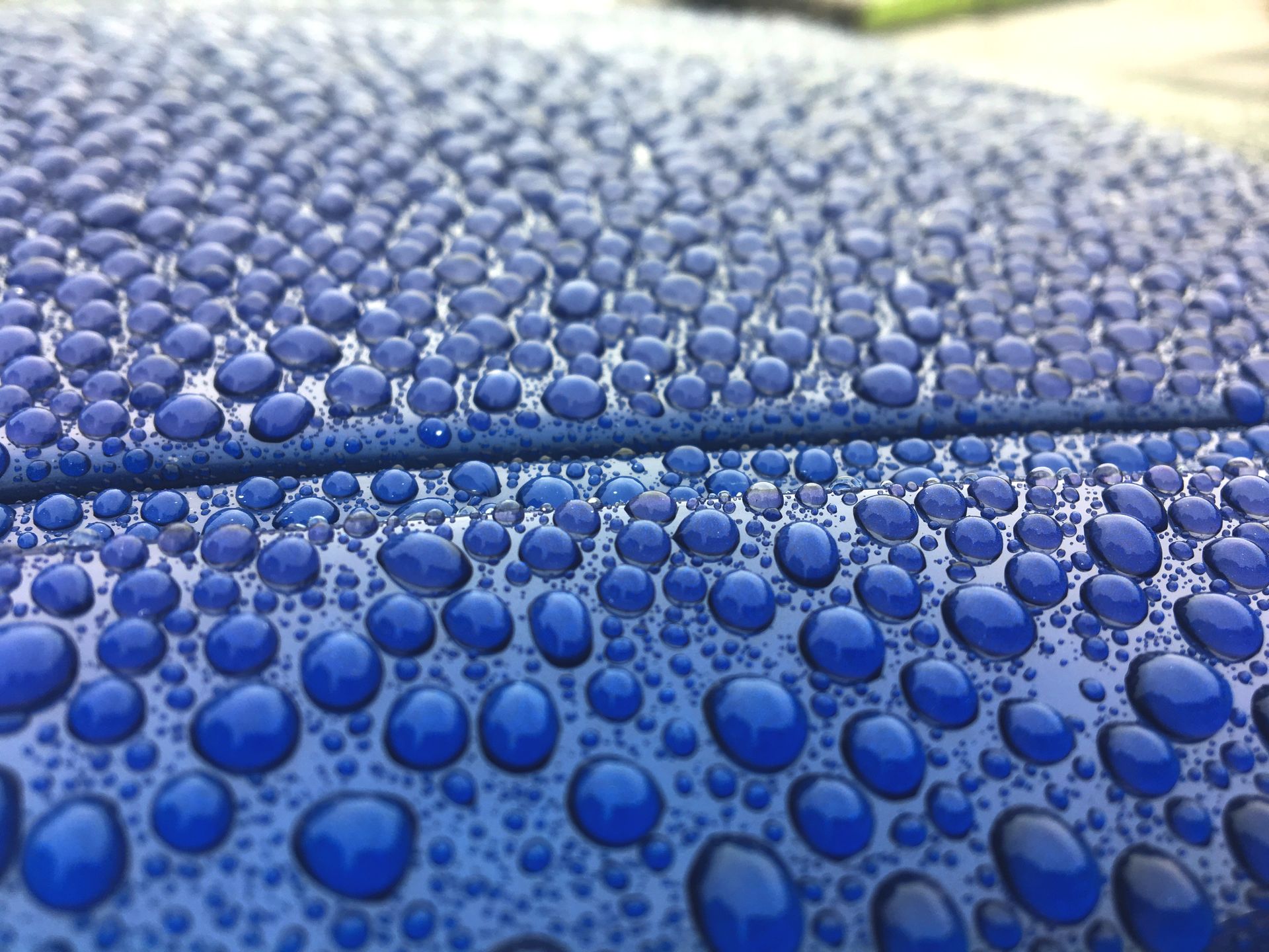 Blue car surface covered in water droplets.