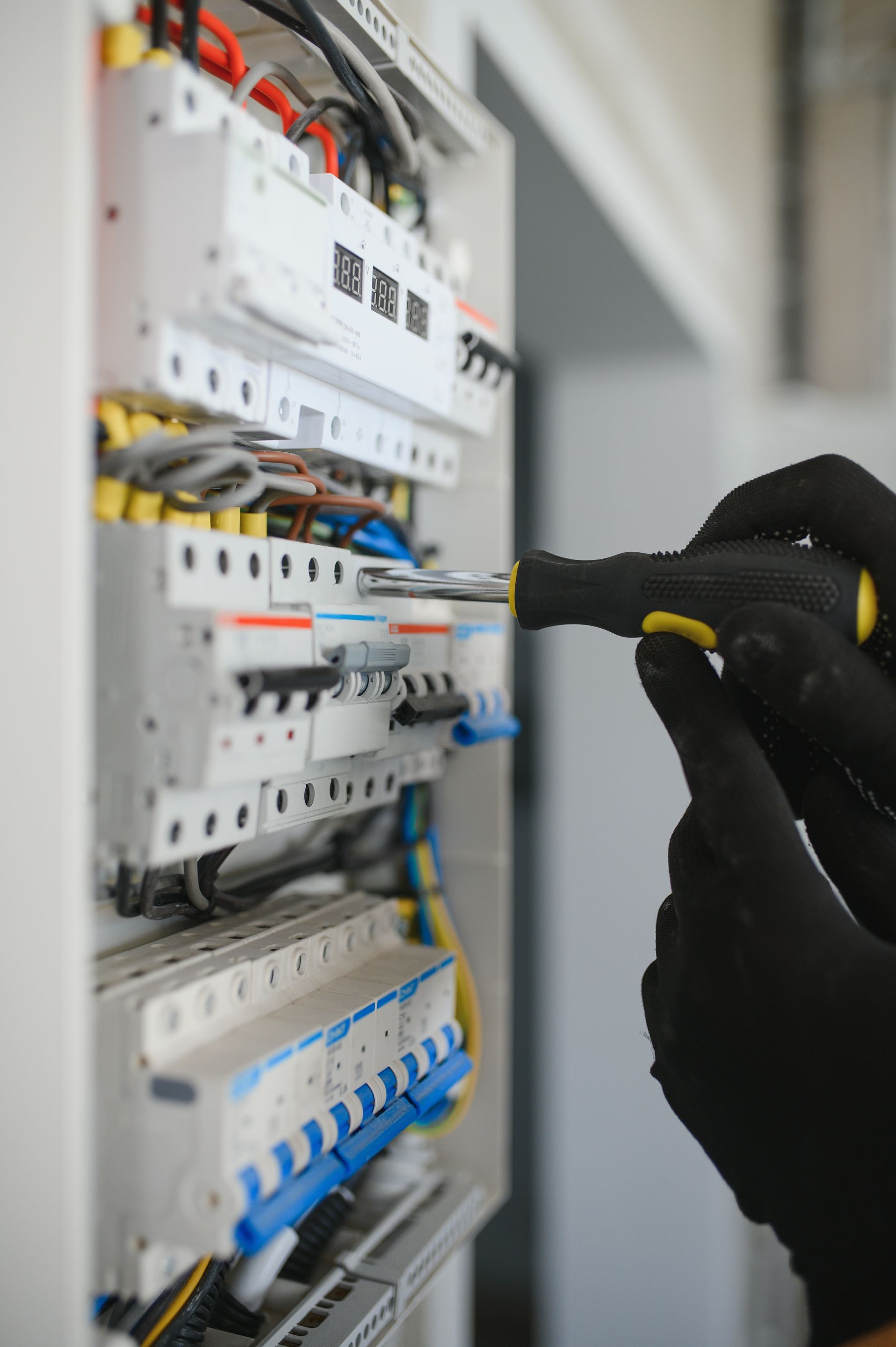 Hands in black gloves working on an electrical panel with a screwdriver.