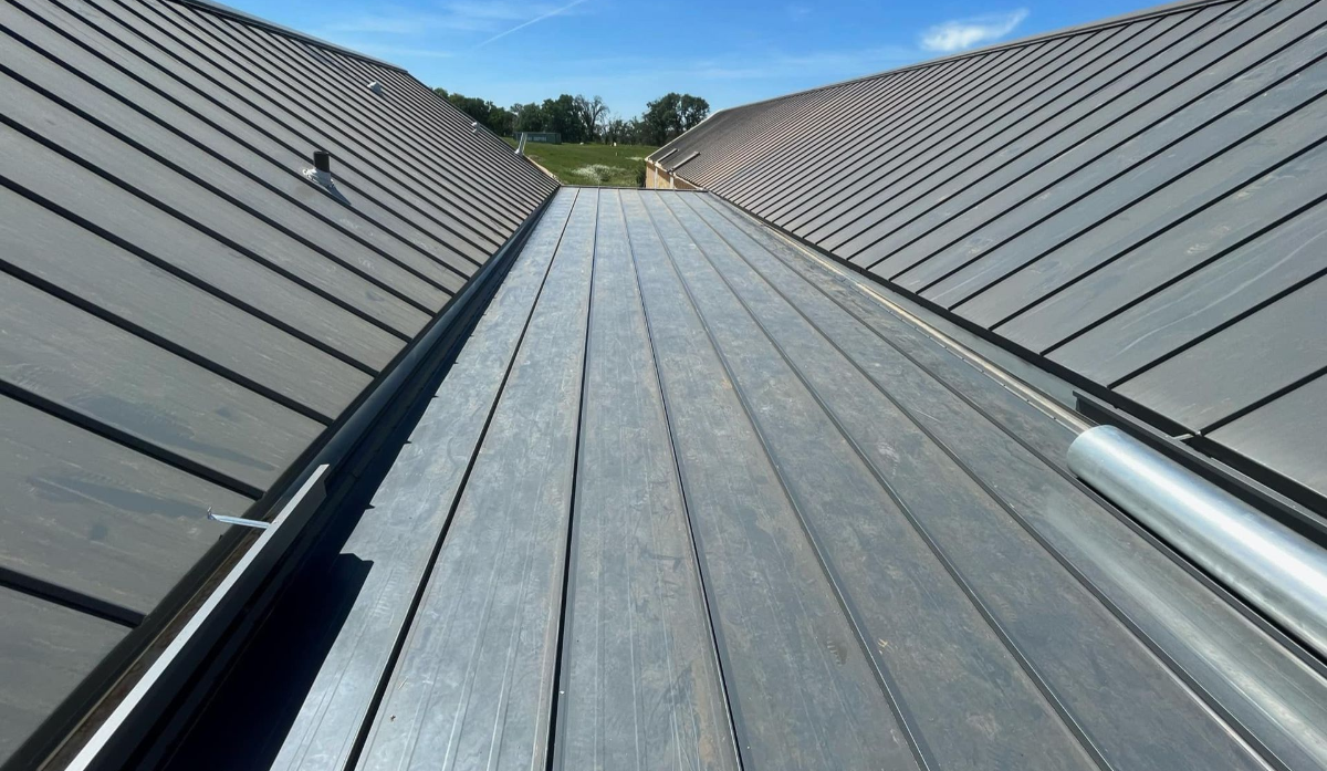 View from a roof gutter with wooden planks, flanked by gray metal roofing. Blue sky in background.