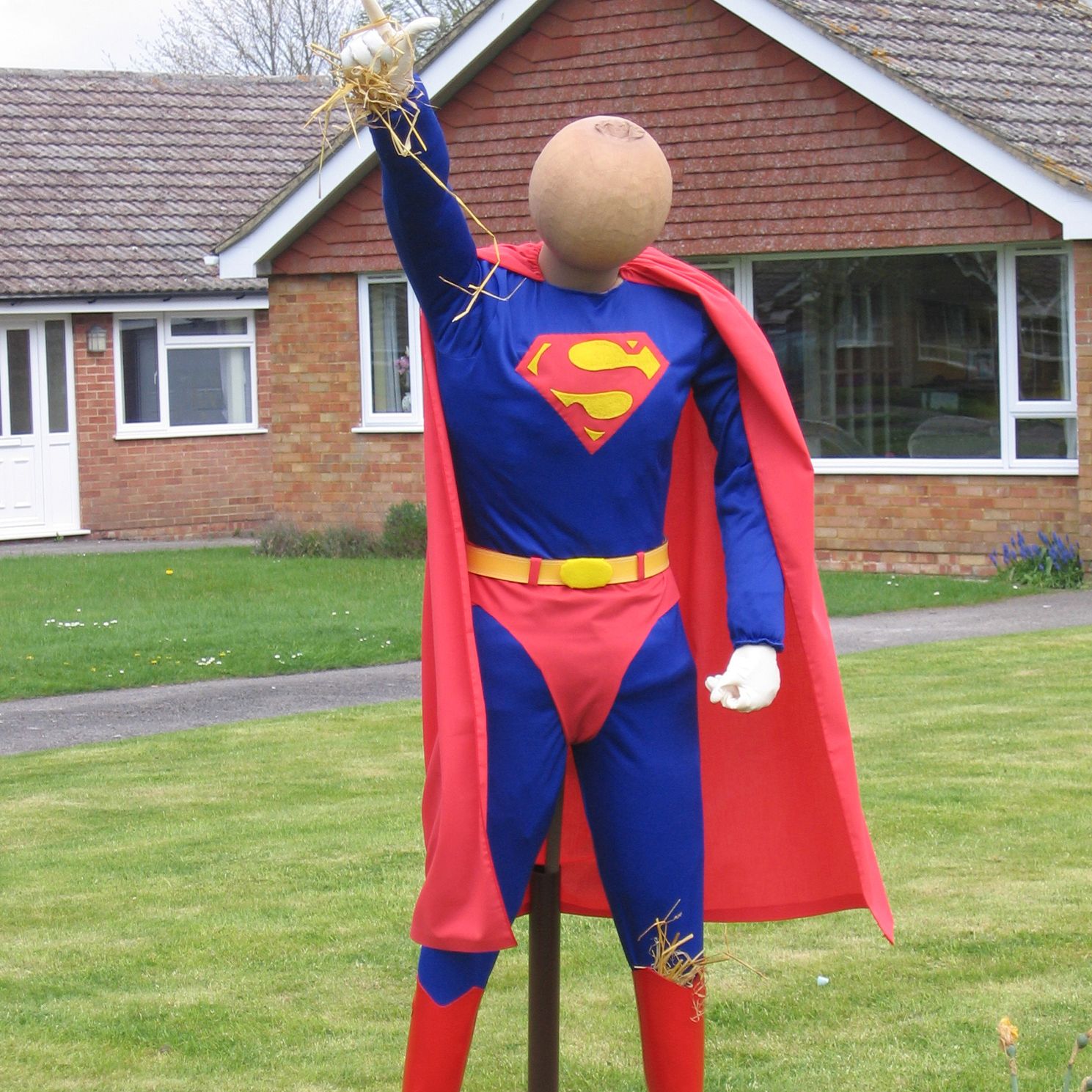 A scarecrow in a superman costume is standing in front of a house