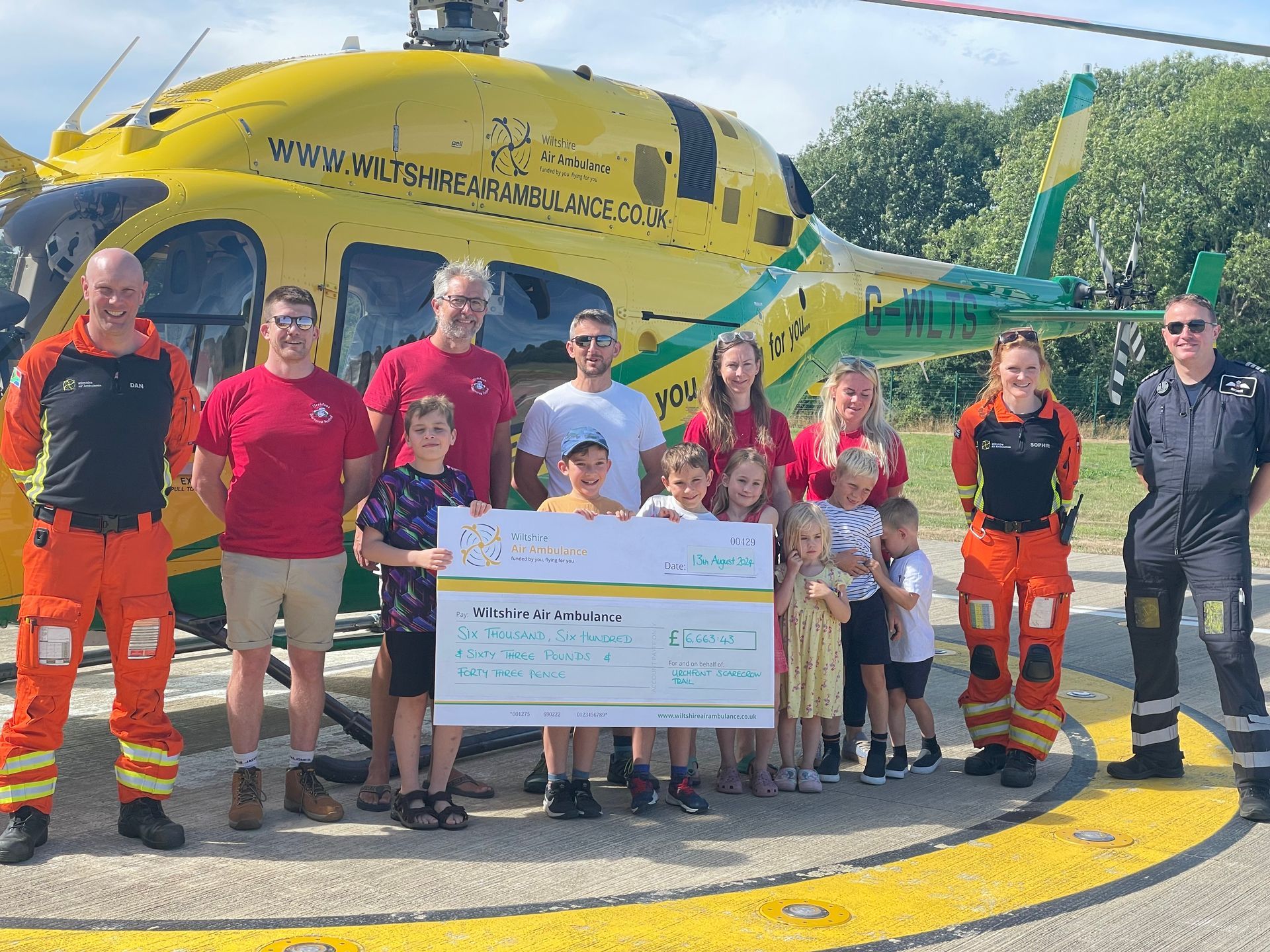 Urchfont Scarecrow Festival trustees present a £6663 donation in front of the helicopter ambulance