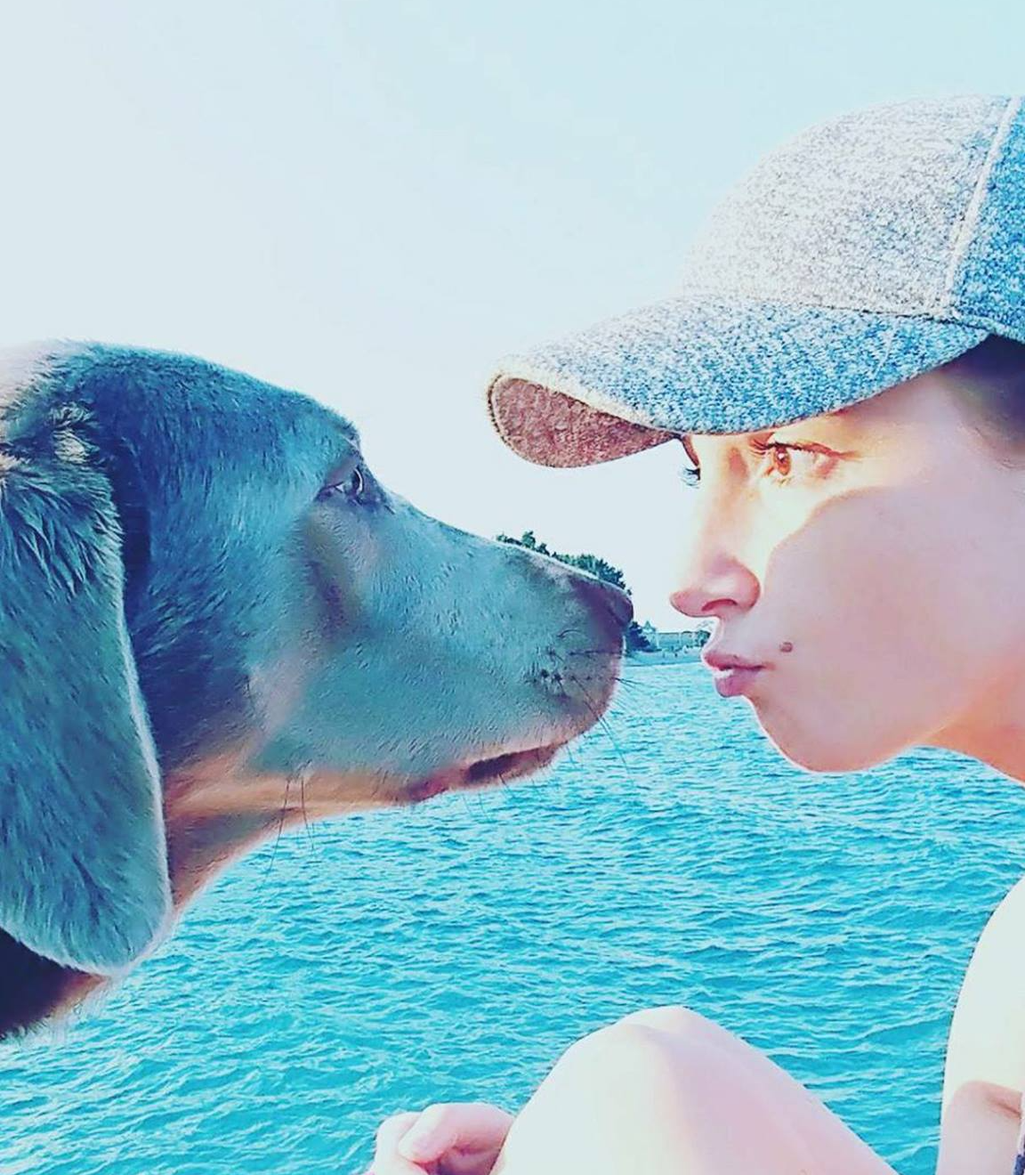 A woman wearing a hat and a Labrador looking at each other