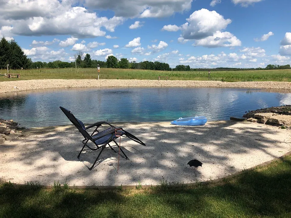 A chair is sitting on the sand next to a pond.