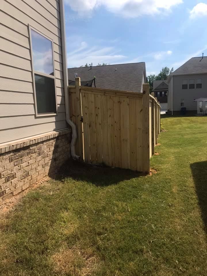 Wooden fence beside a house, built on grass with blue sky in background.