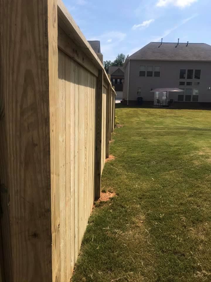 Wooden fence along a grassy backyard, sunny day. A house is in the background.