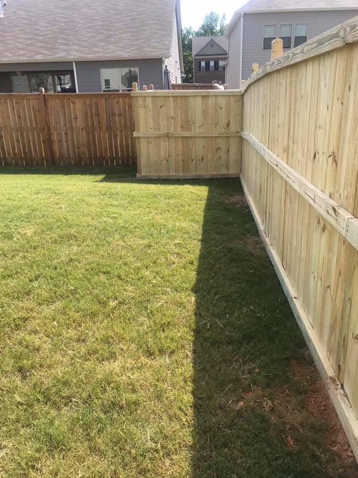 A wooden fence borders a green grassy yard; a section is stained brown, the other side is natural wood.