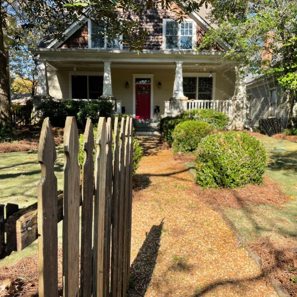 A house with a red door, porch, and a gravel walkway leading from a wooden fence.