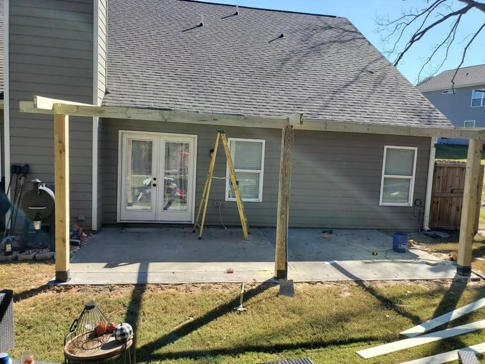 Patio under construction with support beams, next to a house with French doors and windows.