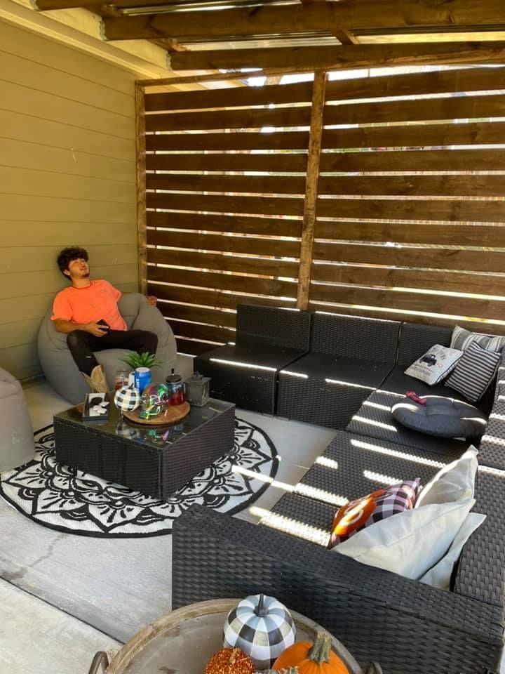 Person relaxing on a beanbag chair in an outdoor lounge area with wicker furniture and a decorative rug.