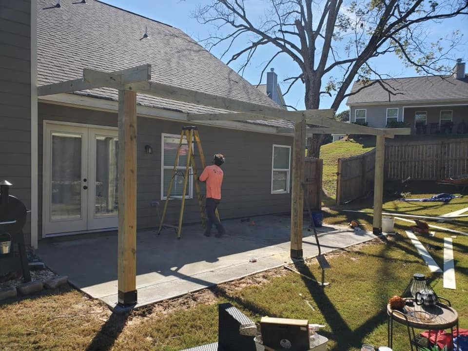 Man on ladder building a wooden patio cover on a sunny day.