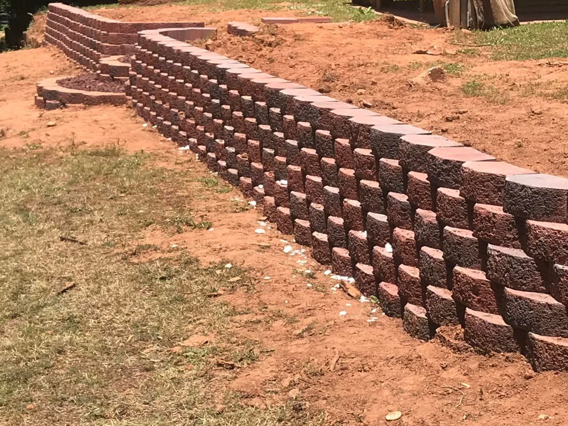 Red brick retaining wall on a red dirt slope, beside grass.