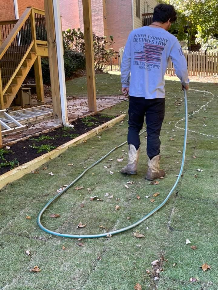 Person in boots holding a hose, outlining a shape on the grass in a backyard.