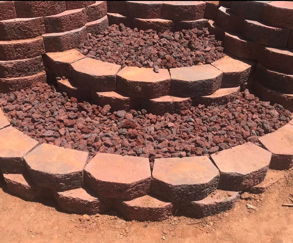 Stone retaining wall in a circular pattern filled with reddish-brown lava rock.