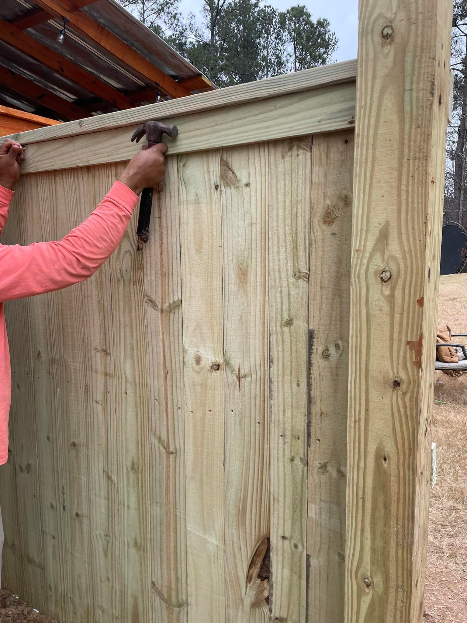 Person hammering trim onto a wooden fence. The fence is made of vertical boards.