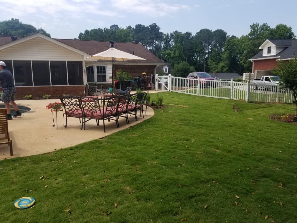 A backyard patio with outdoor seating, a white picket fence, and a grassy lawn.