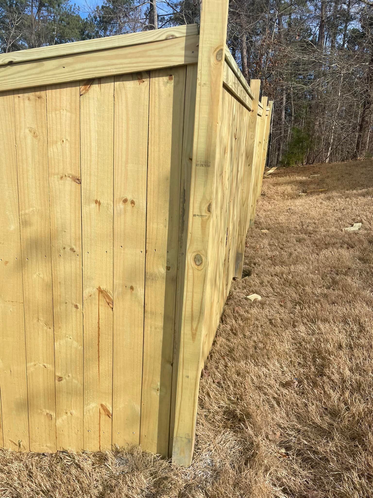 Wooden fence in a yard with dry grass, viewed from a low angle on a sunny day.