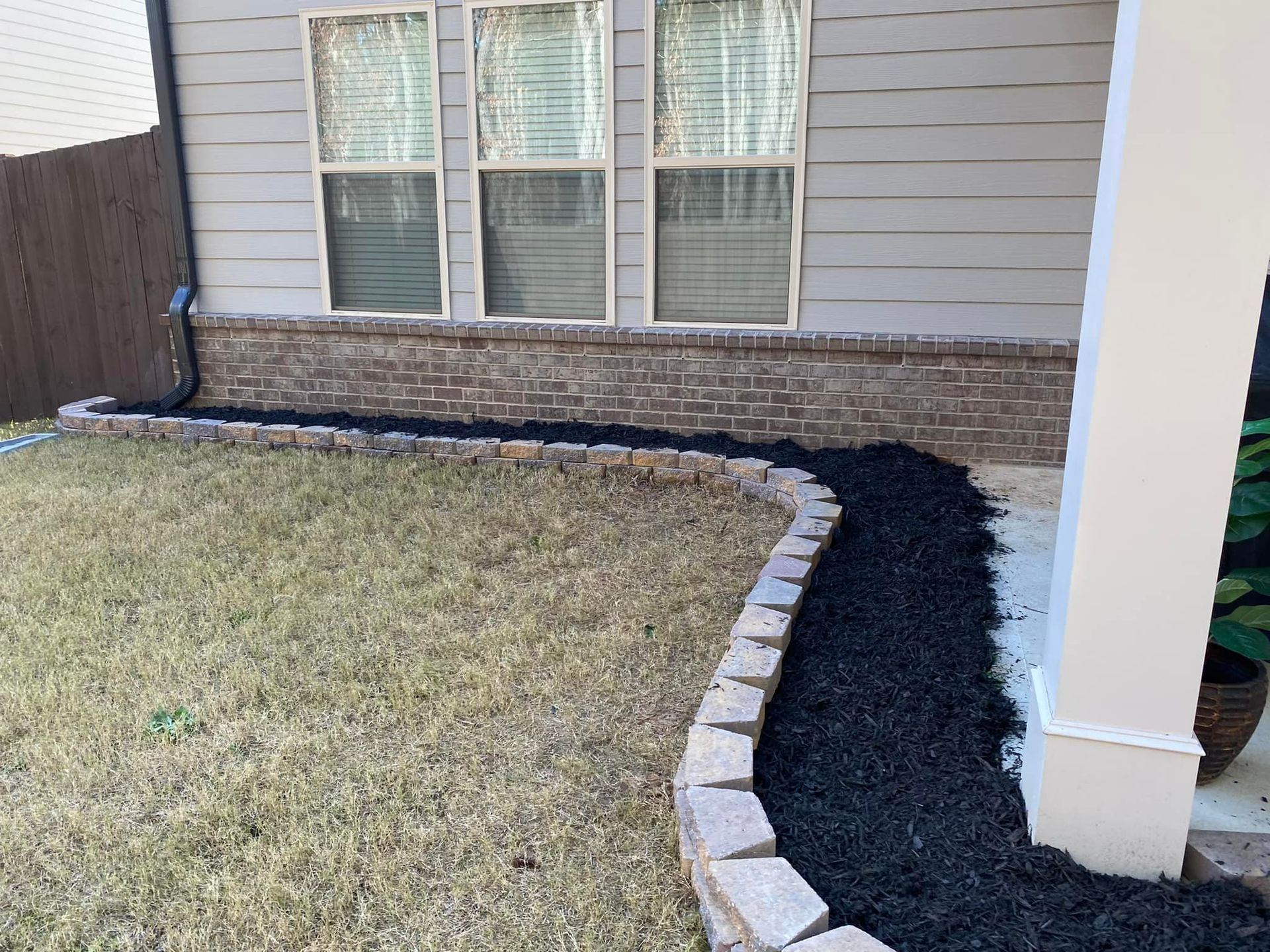 A house exterior with black mulch landscaping bordered by brick edging.