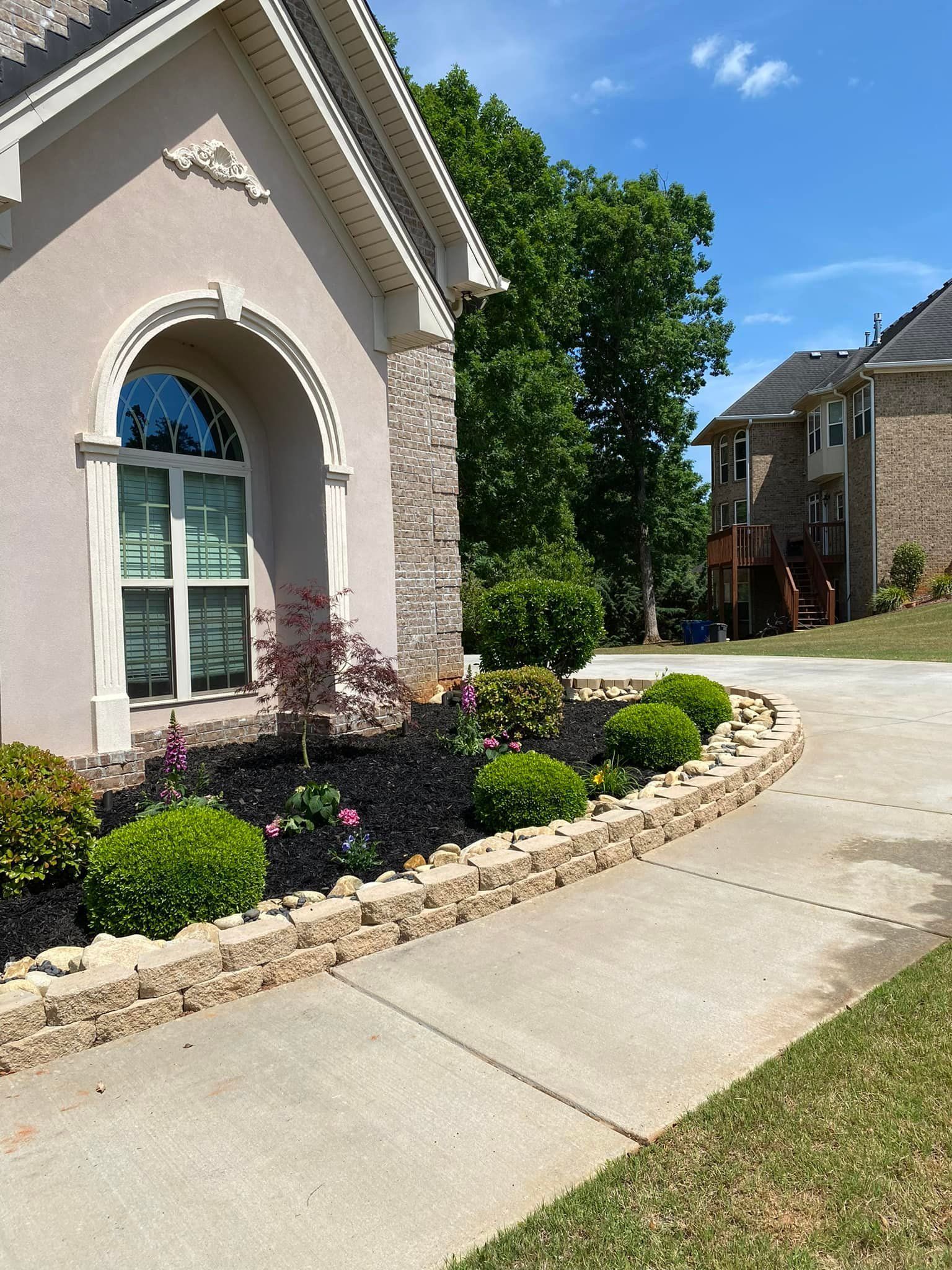 A house with a stone and tan exterior, next to a landscaped garden and a concrete walkway.