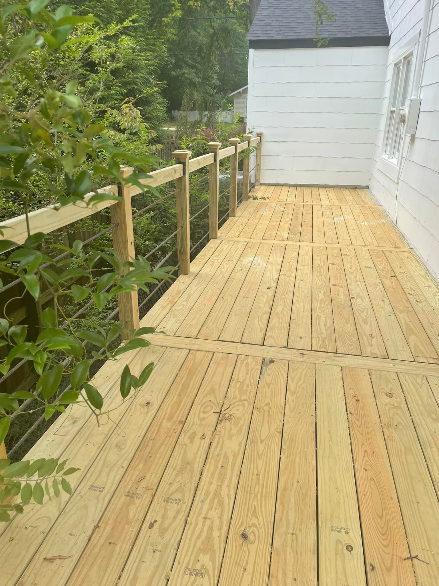Wooden deck with cable railing next to a white building. Green foliage surrounds the deck.