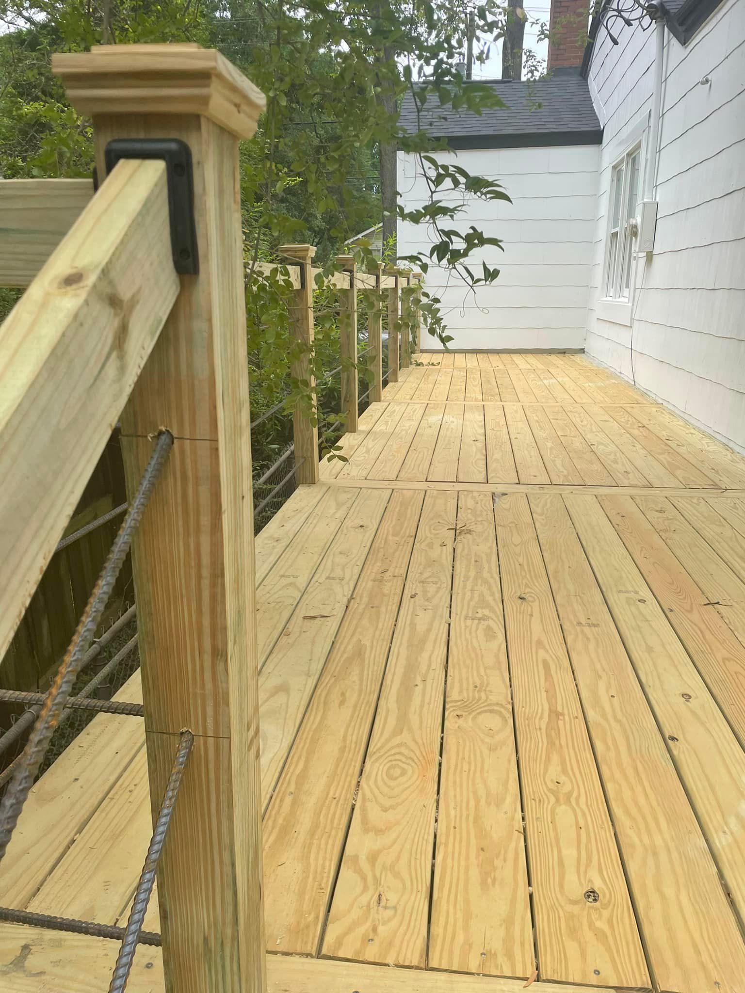 Wooden deck with cable railing next to a white house.
