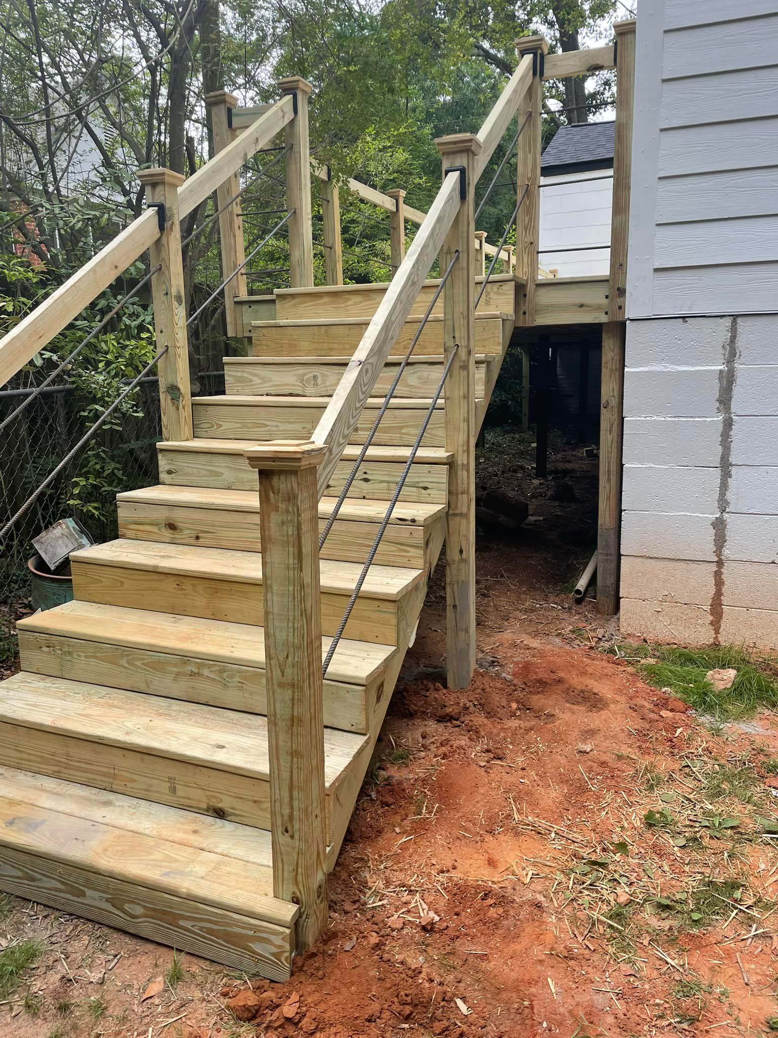 Wooden outdoor stairs with cable railings leading to a deck, next to a building.