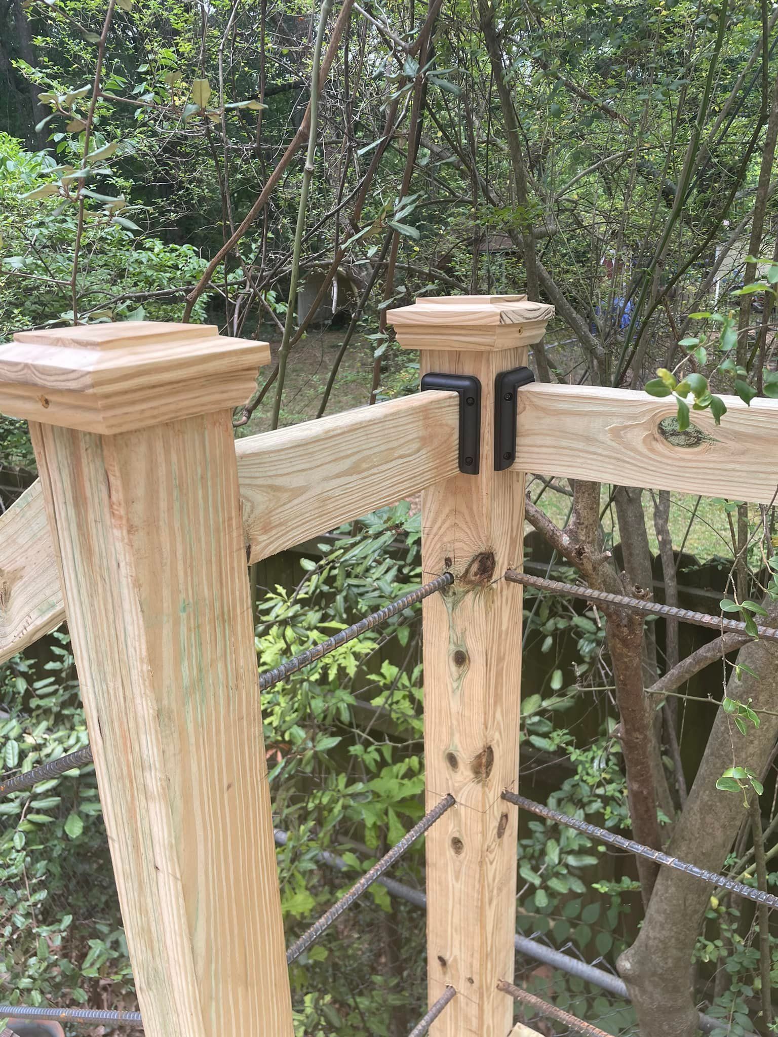Wooden deck railing with black metal corner brackets and cable infill, outdoors.