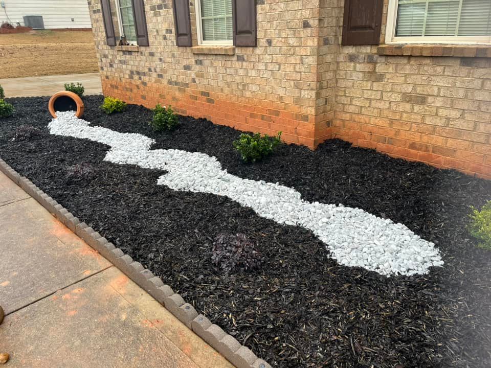 A decorative landscape feature with a faux river of stones, pouring from a terra cotta pot, amidst black mulch.