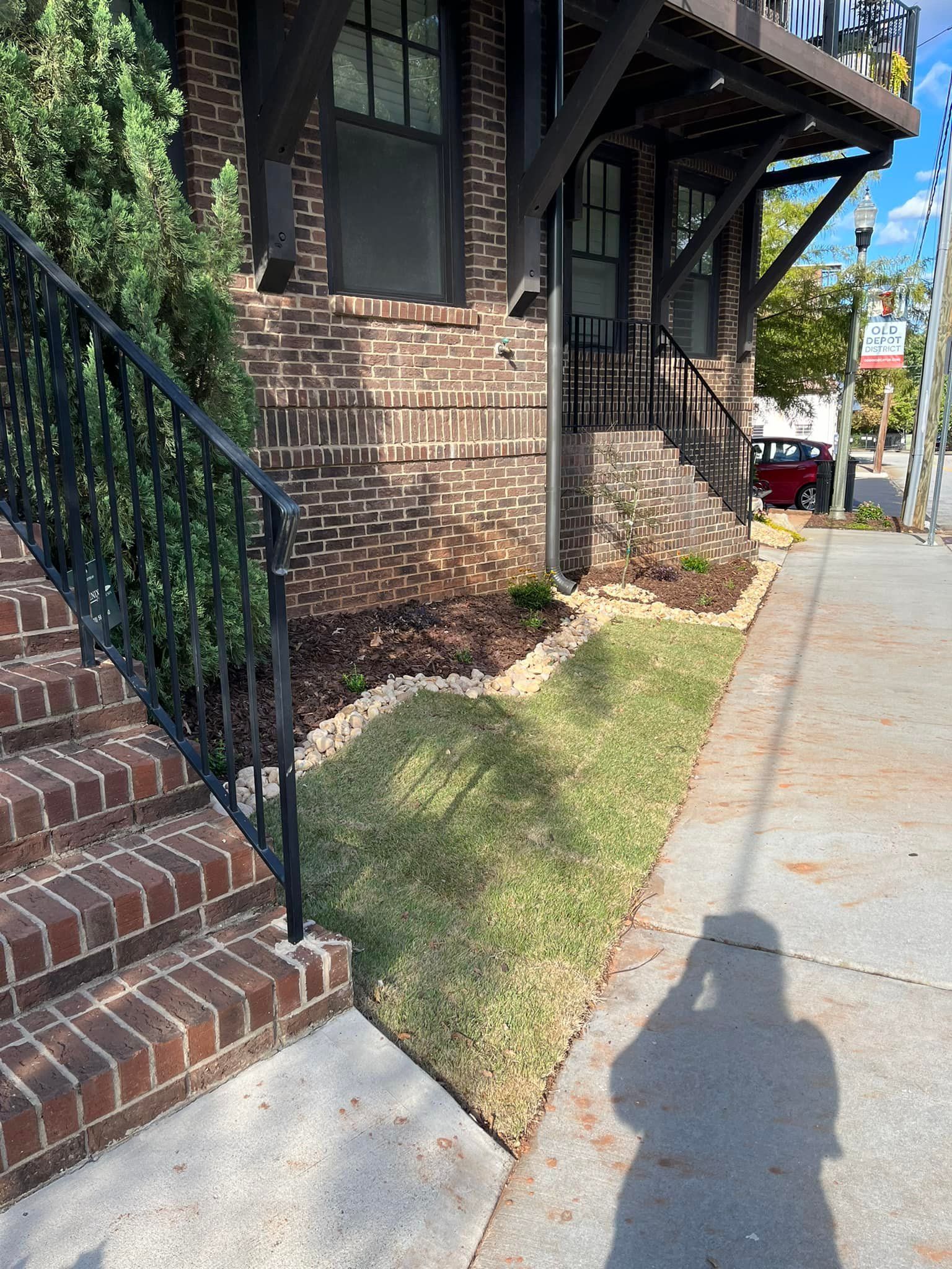 Brick building with steps, lawn, and landscaping; shadow of person taking a photo.
