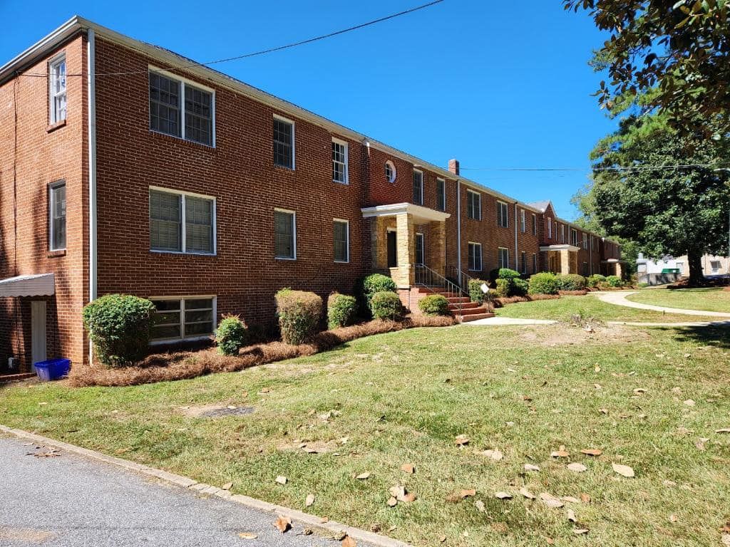 Brick apartment building with green lawn and blue sky.