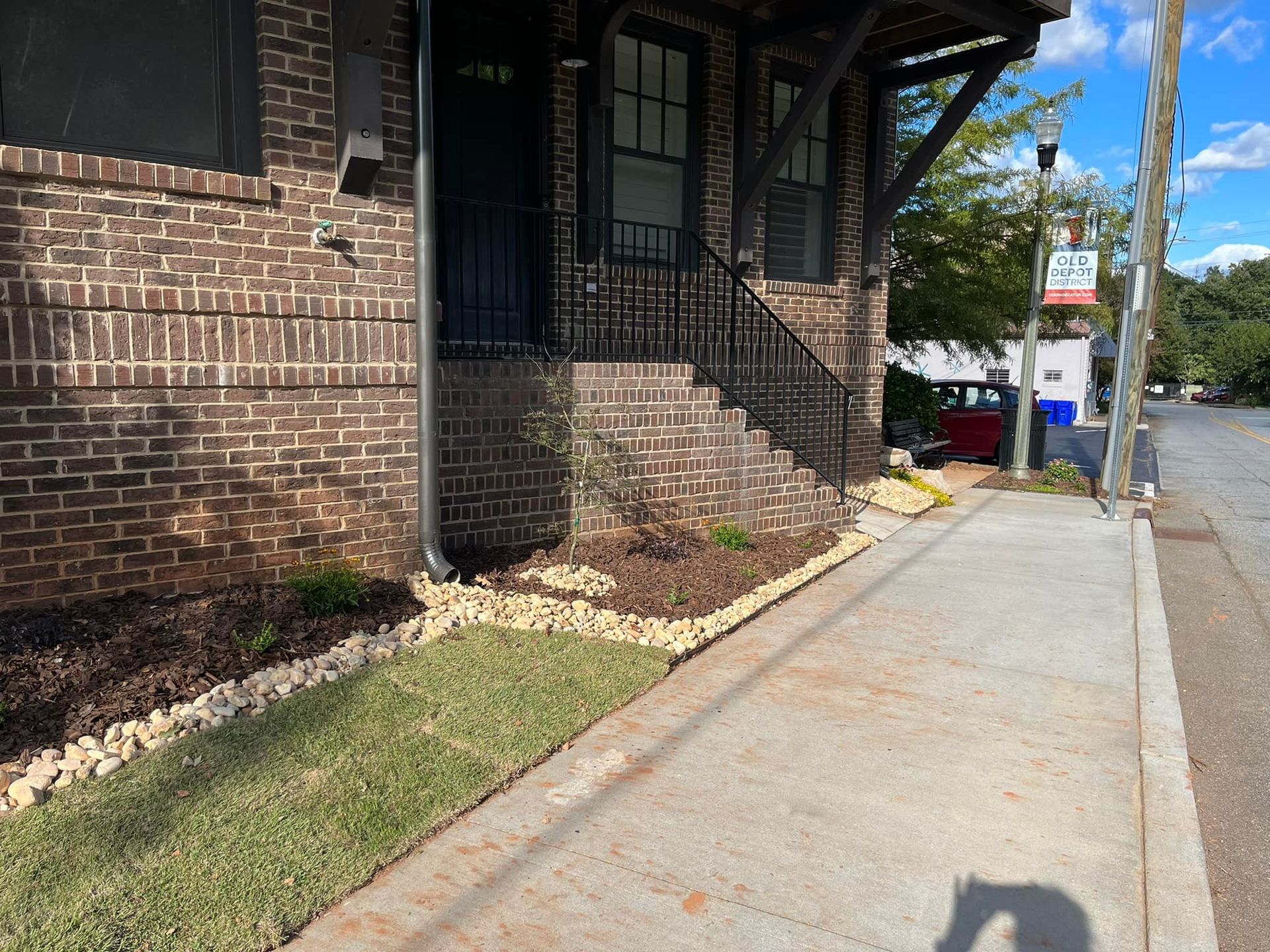 Brick building entrance with stairs, landscaping, and sidewalk.