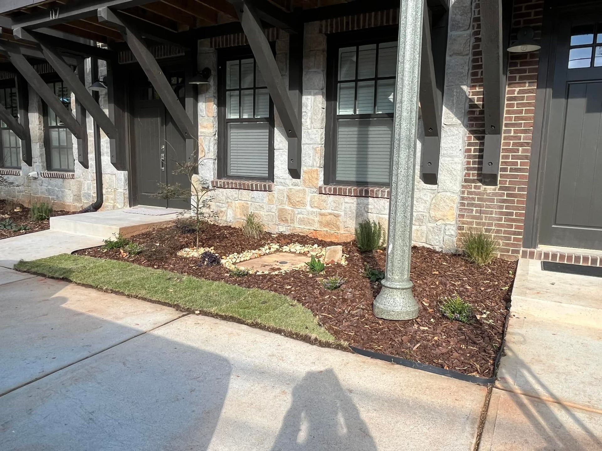 Exterior of townhomes, featuring stone and brick facades with a landscaped area and a light post.