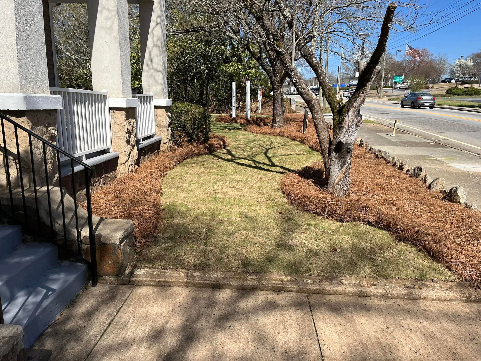 A house exterior with a small lawn, mulch border, and a road in the background.