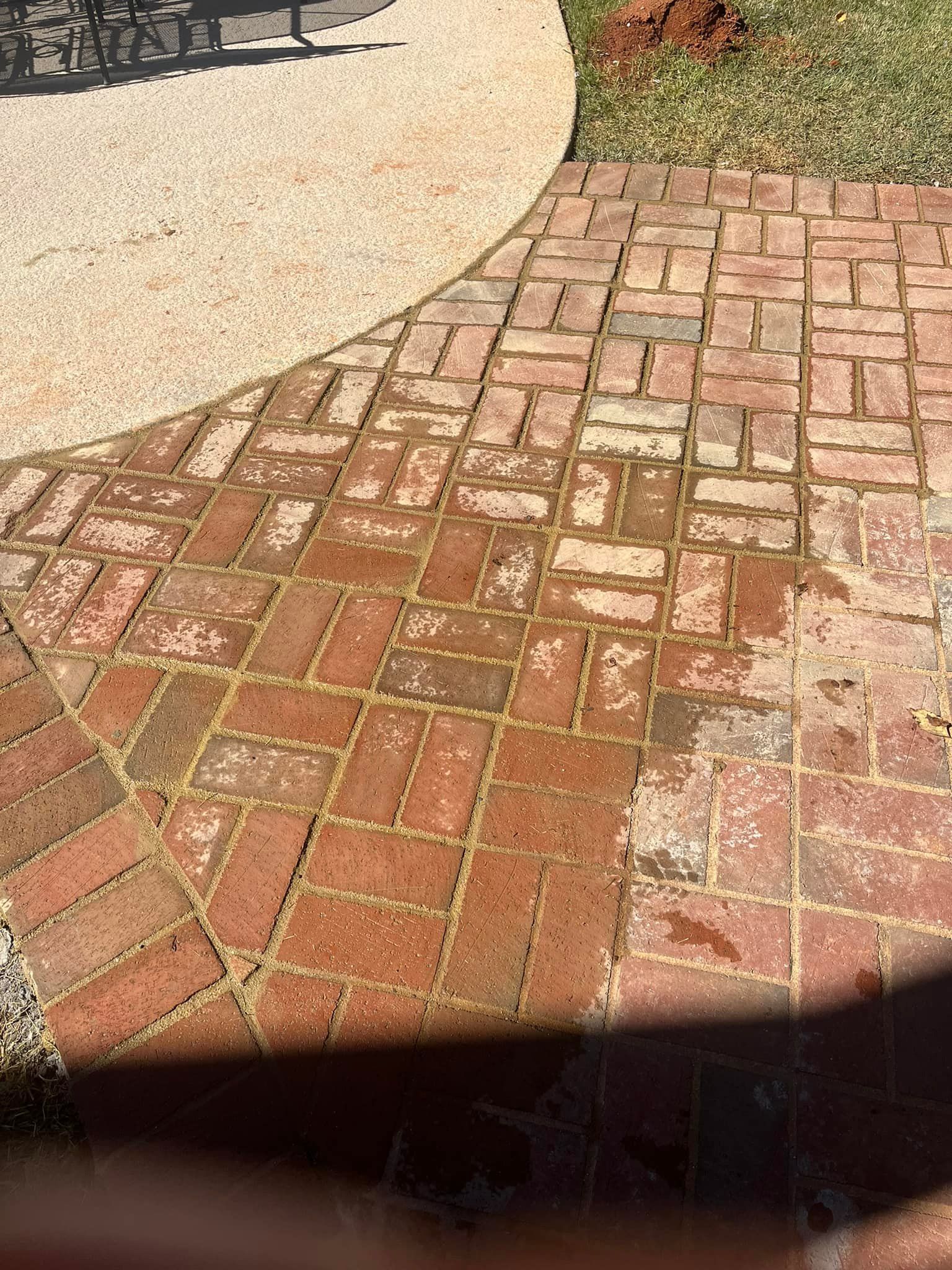 Red brick patio with herringbone pattern adjacent to a concrete pathway and green grass.