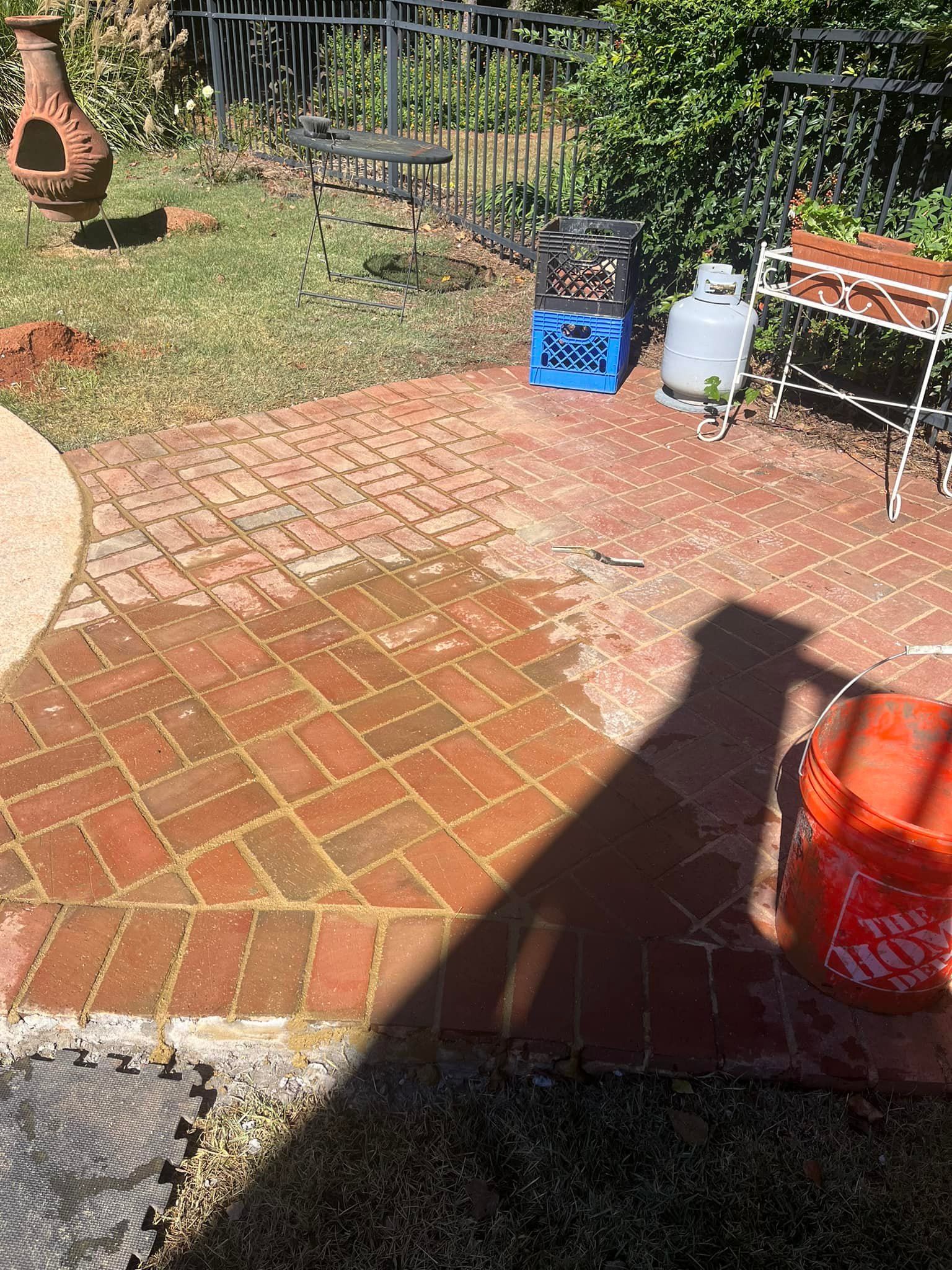 Brick patio with water, propane tank, and shadow. Lawn with a fire pit and blue crate in the background.