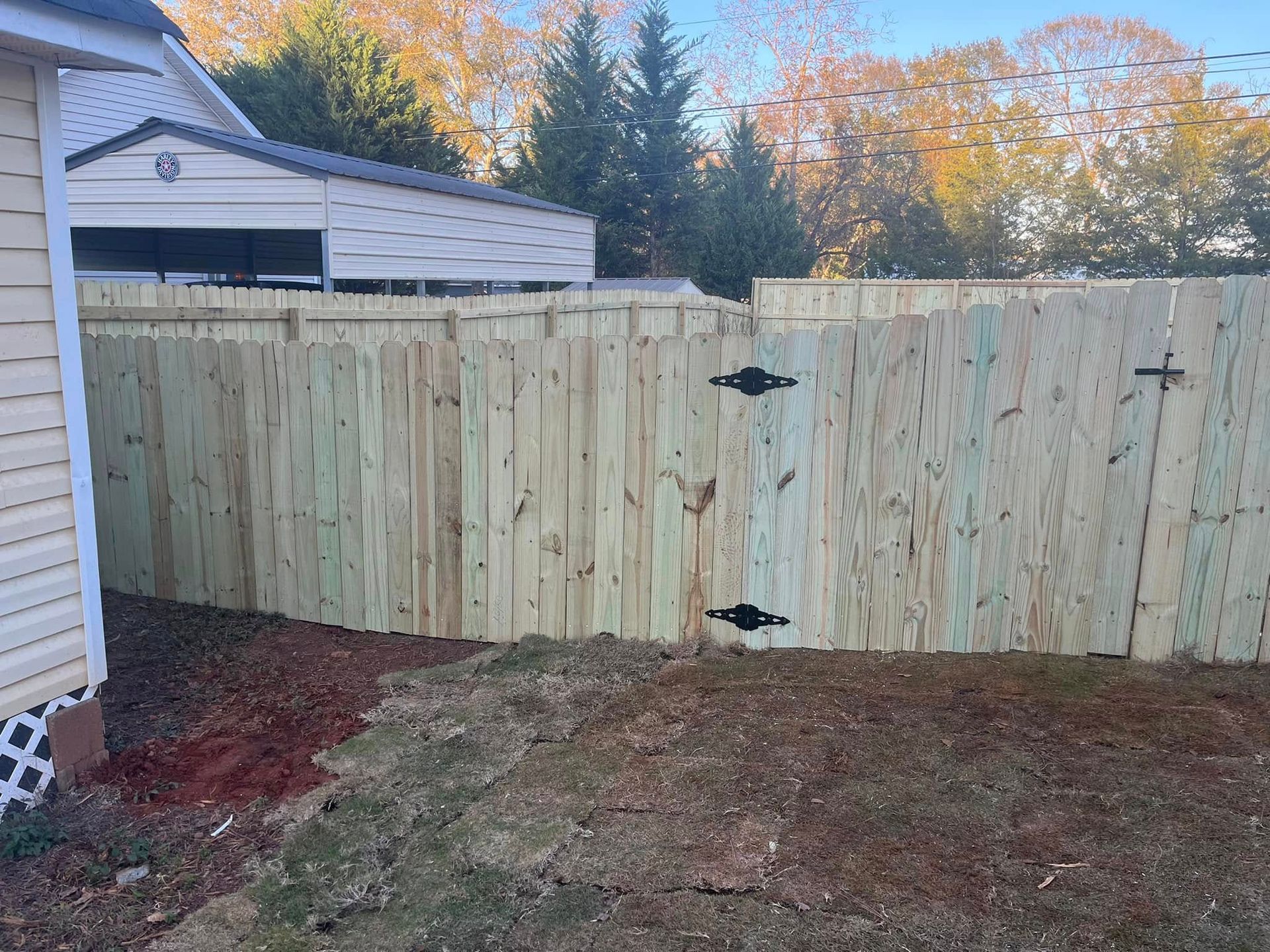 Wooden fence with gate in yard; beige siding on left.