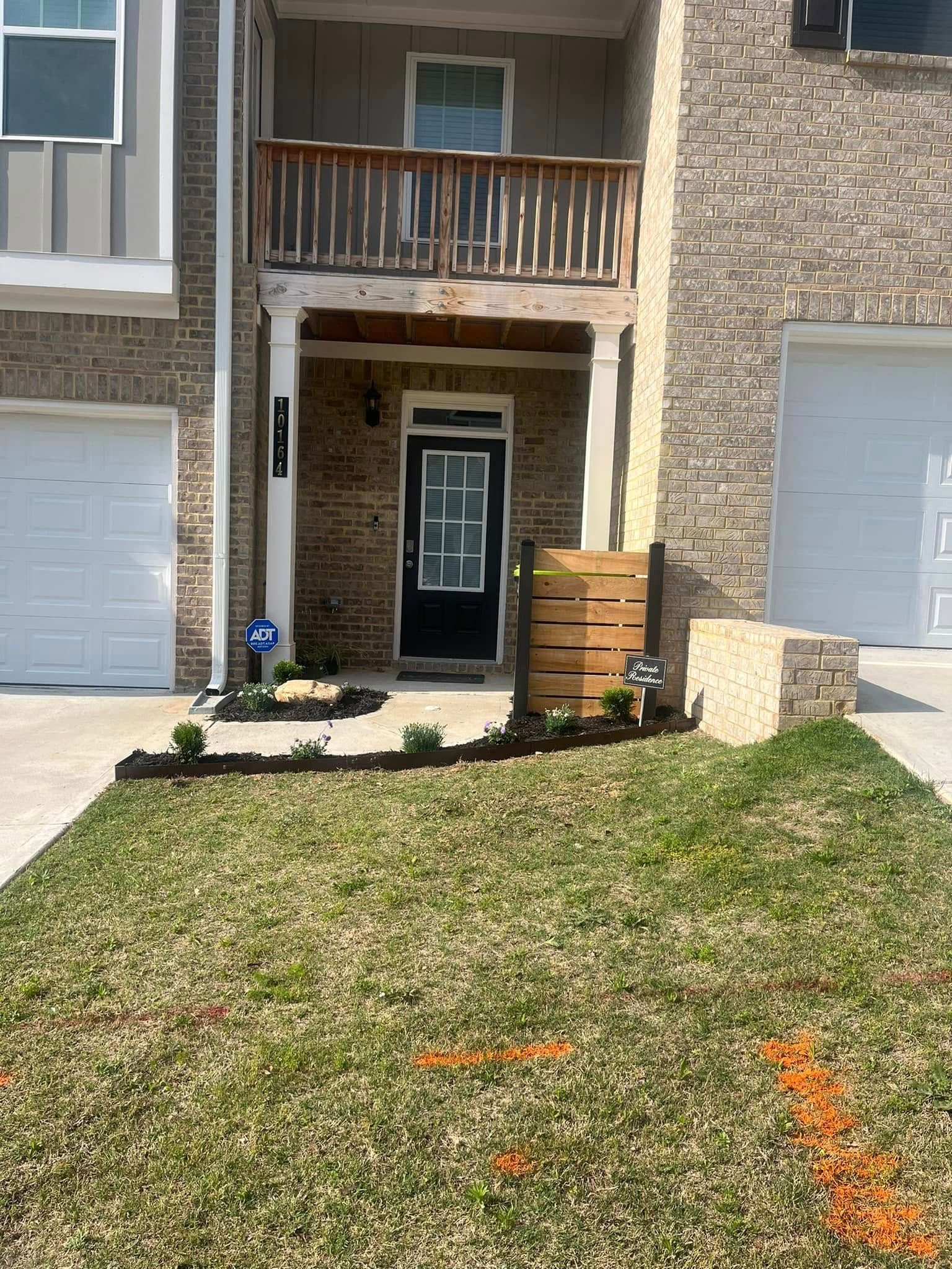 Townhouse exterior with black door, balcony, and front yard landscaping.