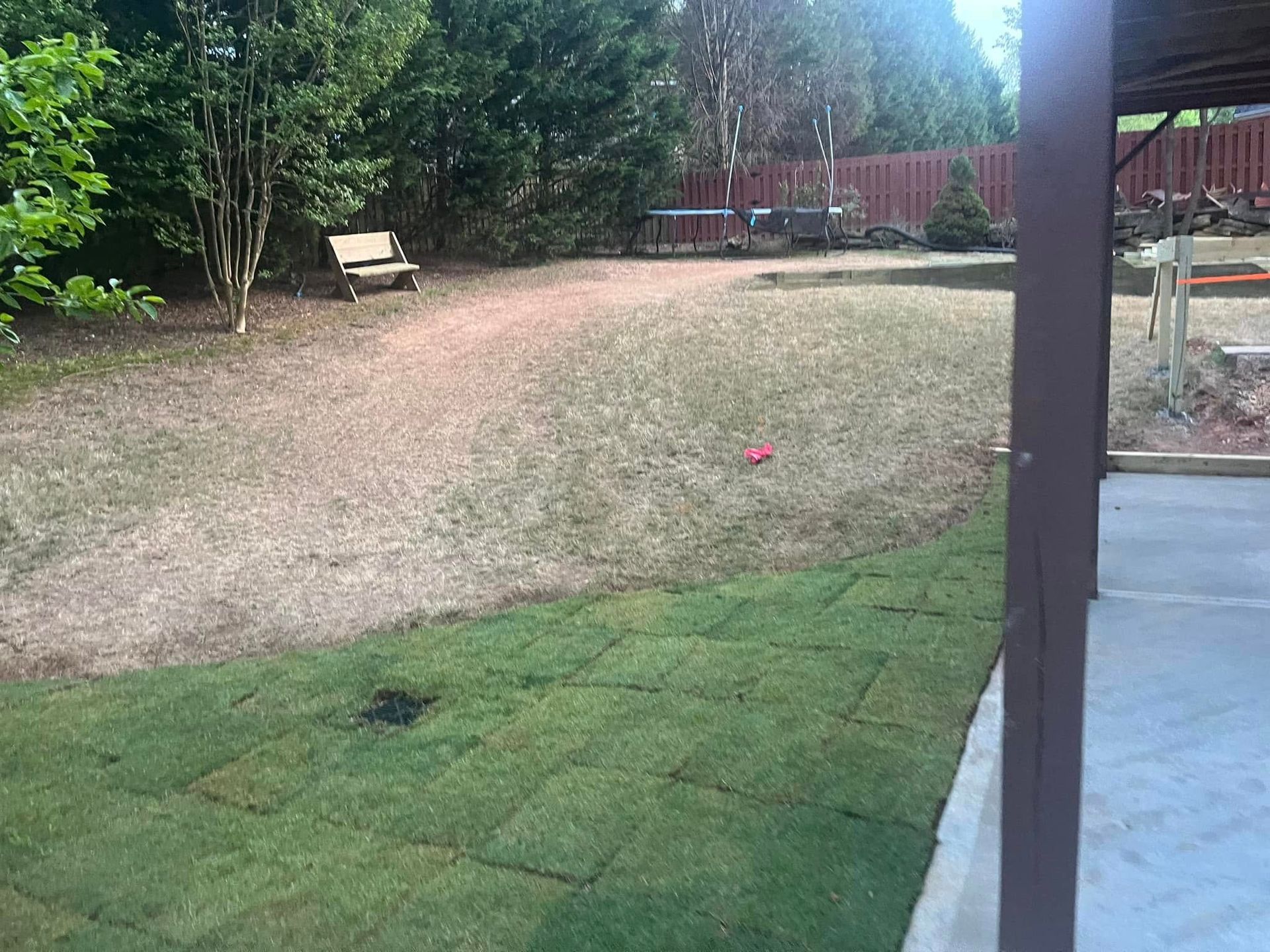Patio with new sod, brown grass, and a bench in a backyard.