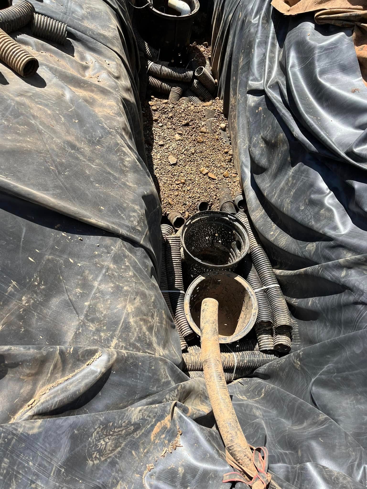 Black tarp lines a trench holding pipes and gravel.