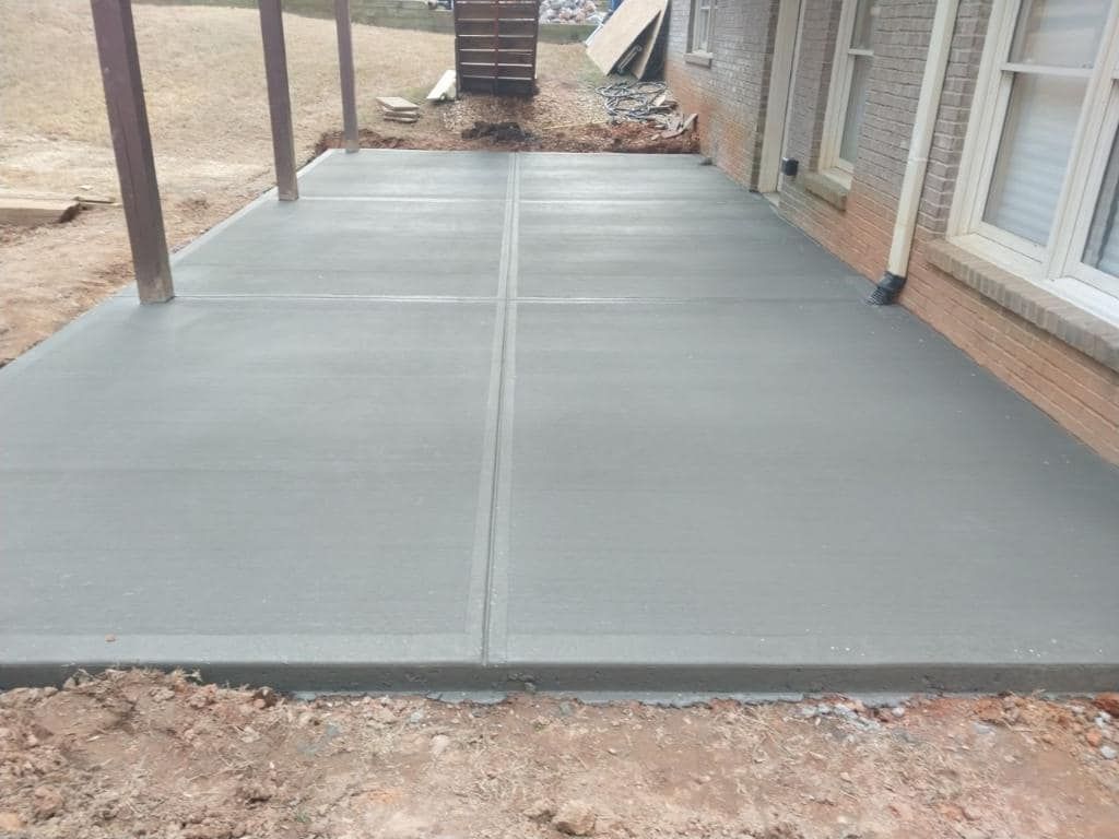 Newly poured concrete patio next to a brick house.